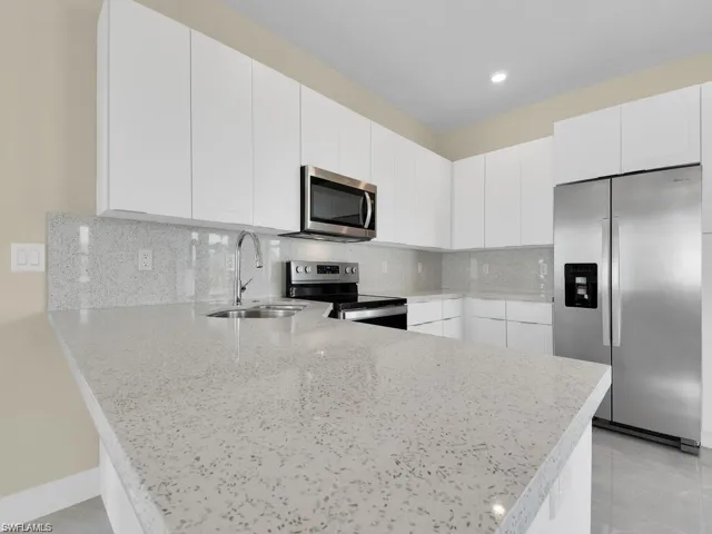 Kitchen with stainless steel appliances, a peninsula, decorative backsplash, white cabinets, and light stone counters