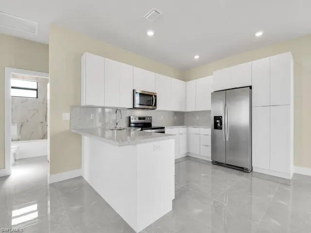 Kitchen with stainless steel appliances, white cabinetry, a peninsula, decorative backsplash, and recessed lighting