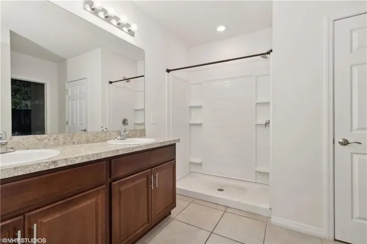 Bathroom featuring a shower, dual vanity, and tile floors