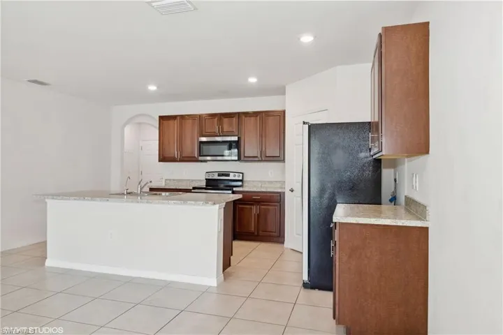 Kitchen featuring a center island with sink, appliances with stainless steel finishes, sink, and light tile flooring