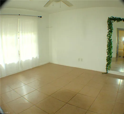 Tiled empty room featuring a ceiling fan and baseboards