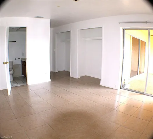 Unfurnished bedroom featuring light tile patterned floors, multiple closets, and ensuite bathroom