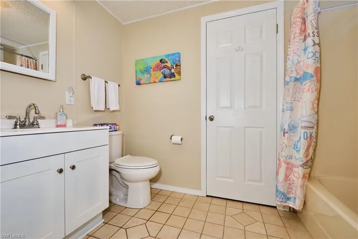 Full bath with tile patterned flooring, baseboards, toilet, vanity, and a textured ceiling
