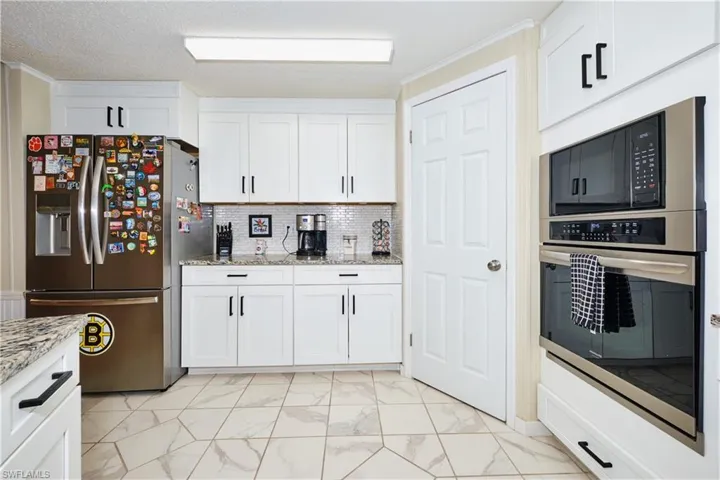 Kitchen featuring light stone counters, stainless steel appliances, marble finish floor, and white cabinets
