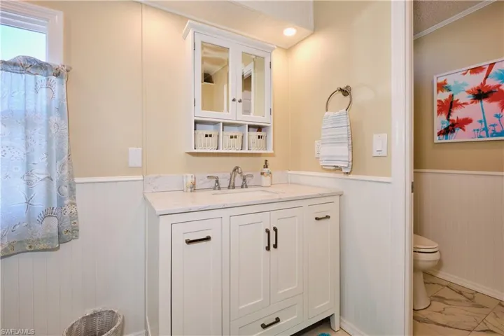 Bathroom featuring vanity, toilet, marble finish floor, and wainscoting