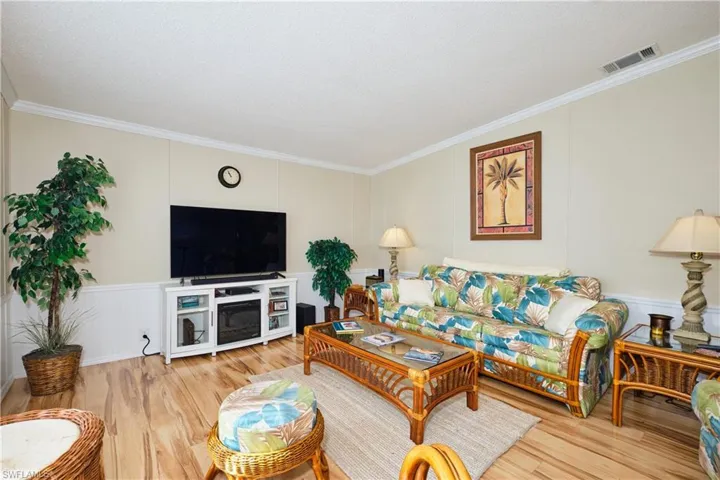 Living room featuring visible vents, a wainscoted wall, wood finished floors, and ornamental molding