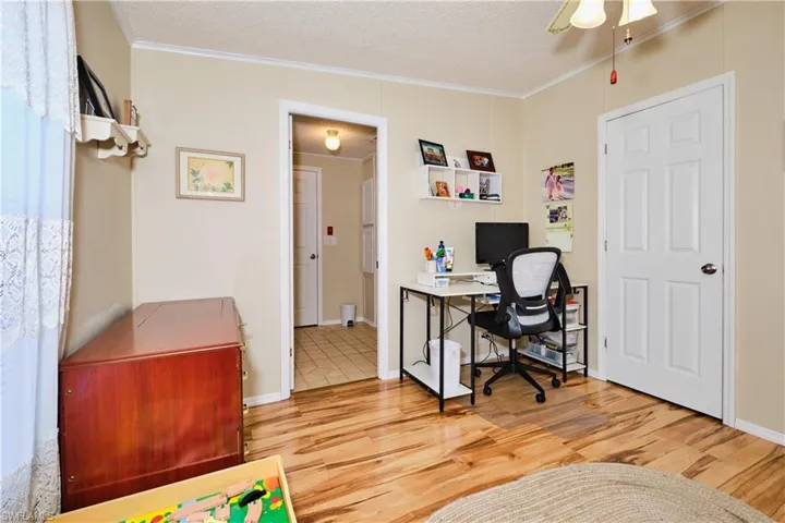Office space featuring wood finished floors, a ceiling fan, baseboards, ornamental molding, and a textured ceiling