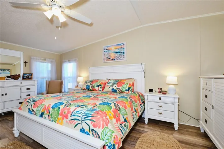 Bedroom with dark wood-style floors, crown molding, and lofted ceiling
