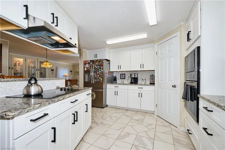 Kitchen featuring light stone countertops, under cabinet range hood, white cabinets, marble finish floor, and stainless steel appliances