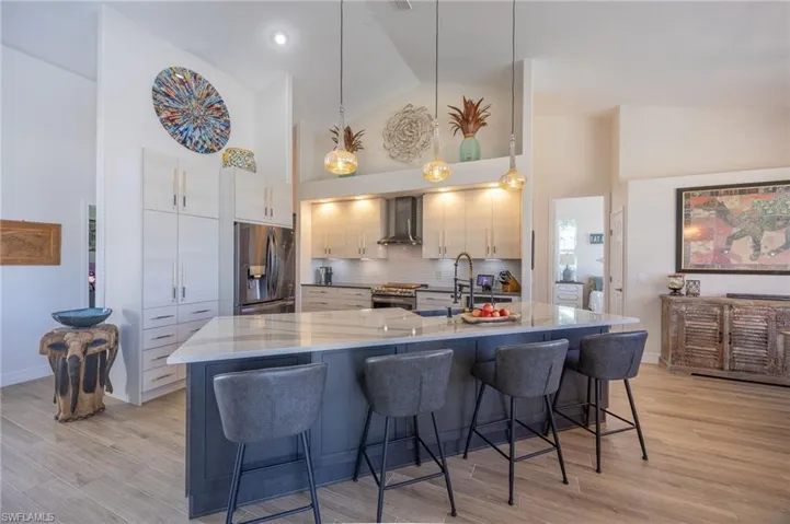 Kitchen featuring hanging light fixtures, a kitchen breakfast bar, stainless steel appliances, light stone countertops, and a large island