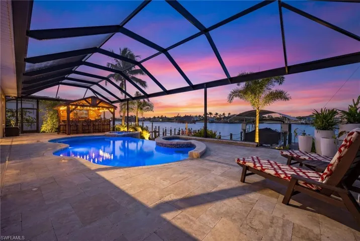 View of swimming pool with a lanai, a water view, a pool with connected hot tub, a sunroom, and a patio area
