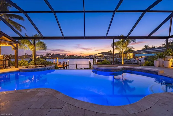 Pool at dusk featuring a pool with connected hot tub, glass enclosure, a water view, and a patio area