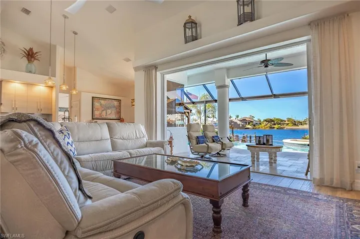 Living room featuring a water view, a ceiling fan, wood-type flooring, a sunroom, and high vaulted ceiling
