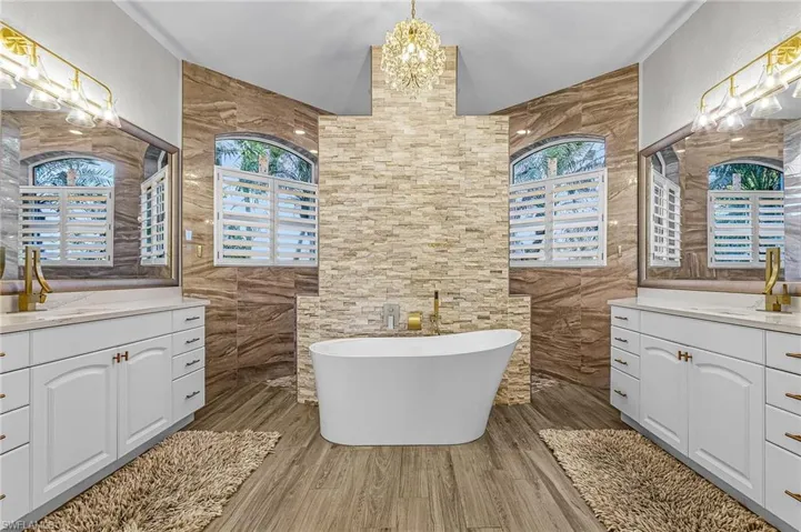 Full bathroom featuring plenty of natural light, a soaking tub, two vanities, dark wood finished floors, and tile walls