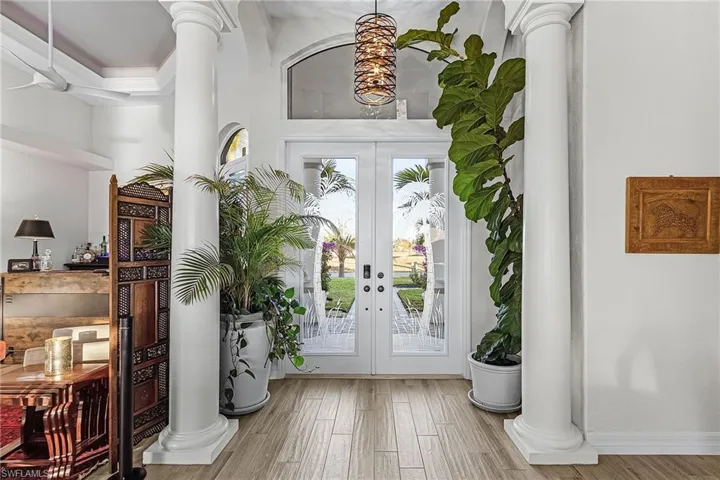 Foyer with decorative columns, french doors, wood finished floors, and crown molding