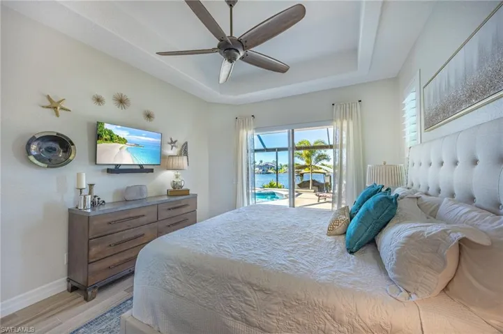 Bedroom featuring access to exterior, light wood-style flooring, a tray ceiling, and ceiling fan