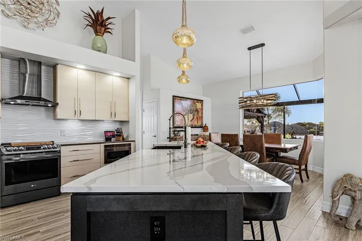 Kitchen featuring a breakfast bar area, appliances with stainless steel finishes, decorative light fixtures, wall chimney exhaust hood, and a center island with sink