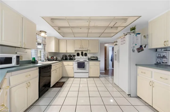 Kitchen featuring sink, light tile patterned floors, white appliances, and cream cabinetry