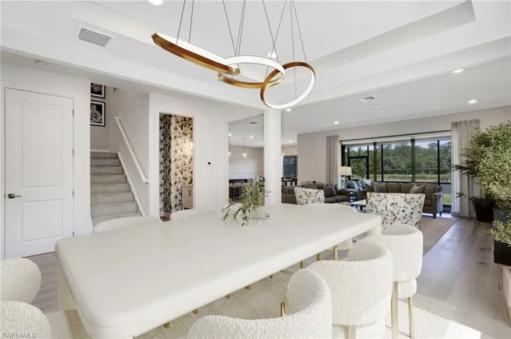 Dining area with visible vents, a tray ceiling, stairway, and light wood-style flooring