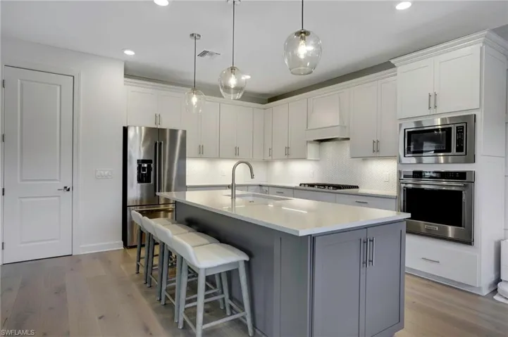 Kitchen with light wood finished floors, stainless steel appliances, visible vents, a sink, and premium range hood