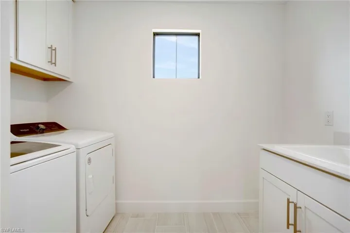 Clothes washing area with cabinet space, baseboards, separate washer and dryer, and a sink