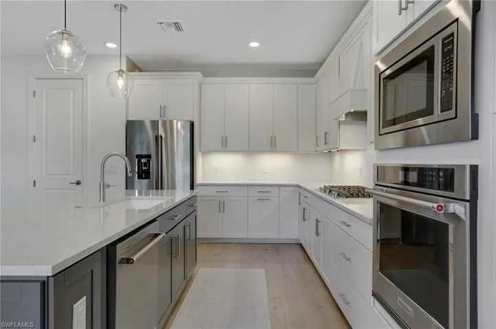 Kitchen with decorative backsplash, hanging light fixtures, stainless steel appliances, light wood-style floors, and a sink