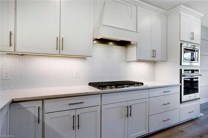 Kitchen with dark wood-style flooring, white cabinetry, appliances with stainless steel finishes, tasteful backsplash, and custom range hood