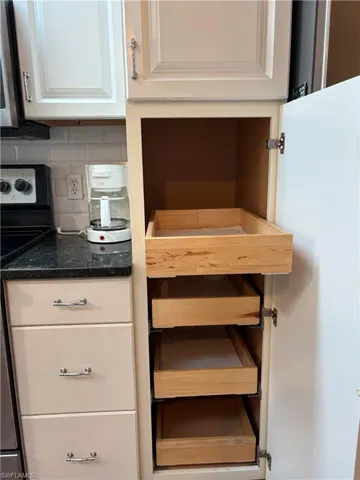 View of Kitchen's Renovated/Upgraded  pull out tray shelves and stainless steel electric stove, white cabinets, decorative backsplash, and dark stone counters