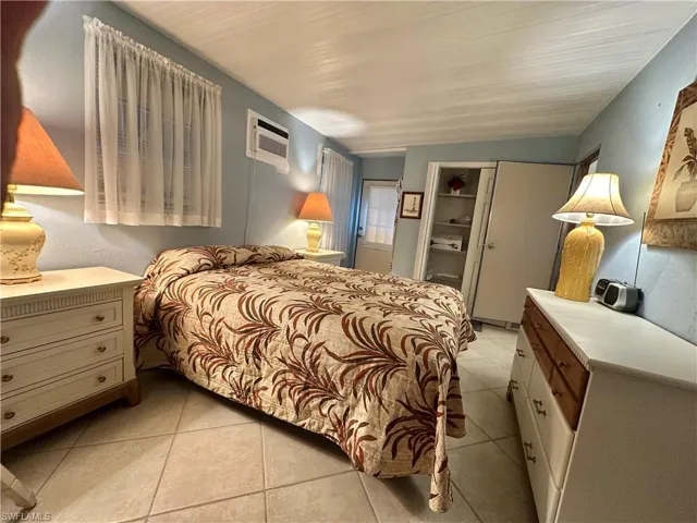 View of rear enclosed lanai with wall A/C used as Bedroom featuring light tile patterned flooring and entry to living room and steel doorway rear entrance