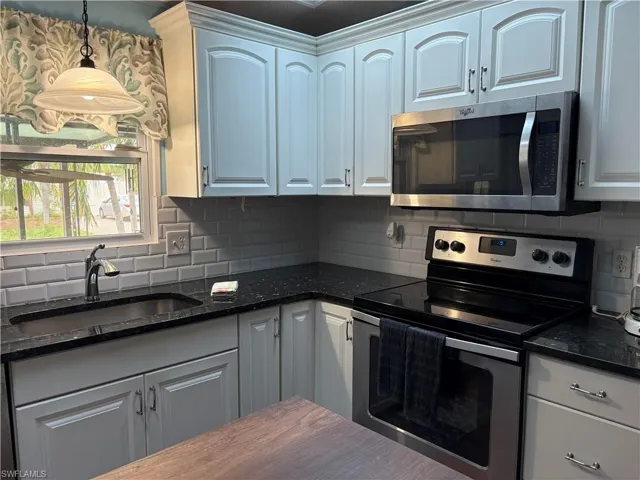 View of upgraded/renovated granite countertop Kitchen with stainless steel appliances, backsplash, dark stone countertops, and decorative light fixtures
