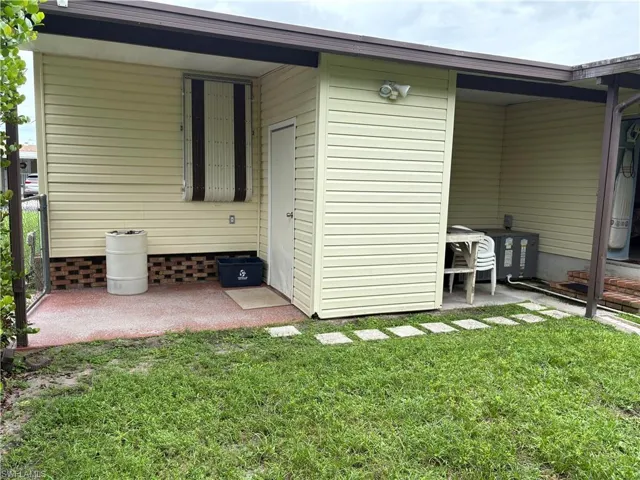 View of rear of property with space for golf cart plug in and entry door to enclosed lanai used as a third bedroom