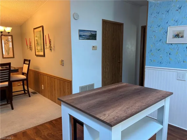View of Kitchen with a center island/stools, textured ceiling, wainscoting, dark wood-type flooring, and wood walls