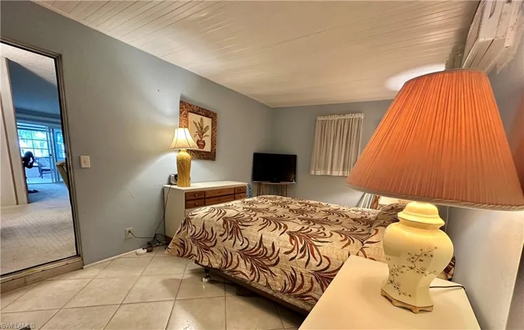 View of large rear enclosed lanai with wall AC used as Bedroom with light tile patterned floors and Enttry door from rear.