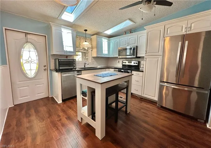 View of upgraded/renovated stainless steel fKitchen boasting finishes, a textured ceiling, pendant lighting, vaulted ceiling, and decorative backsplash with a center island w/stools