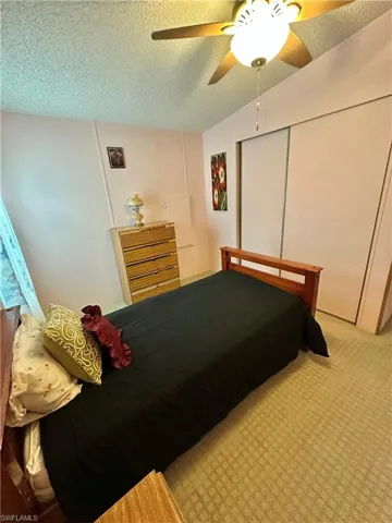 View of good-sized Second Bedroom with a textured ceiling, a slider closet, a ceiling fan