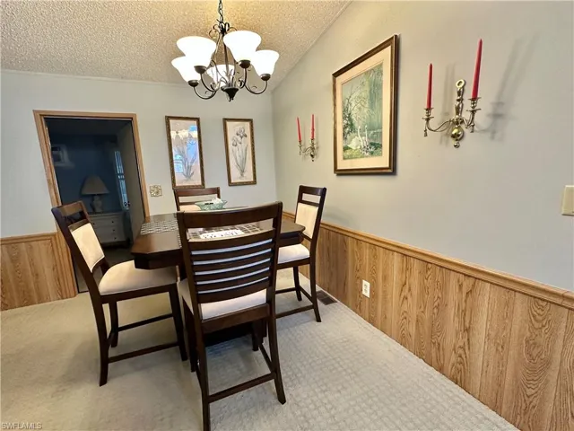 View of Dining area with a Bistro table [expandable] featuring wooden walls, a wainscoted wall, a textured ceiling, a chandelier