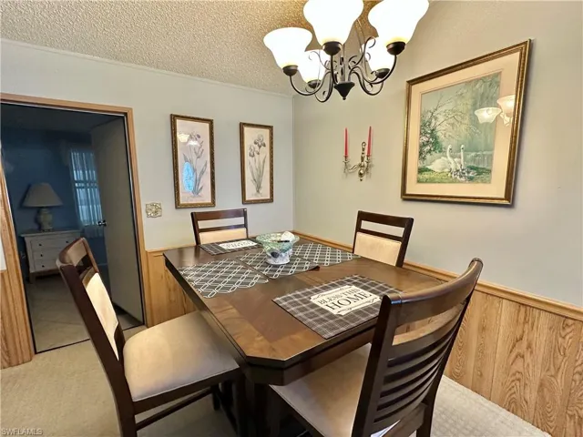 View of Dining room's Bistro expandable table with wainscoting, wood walls, a textured ceiling, a chandelier, and crown molding