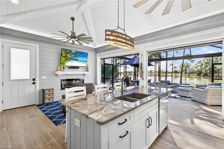 Kitchen with open floor plan, light stone countertops, white cabinetry, a kitchen bar, and a sunroom