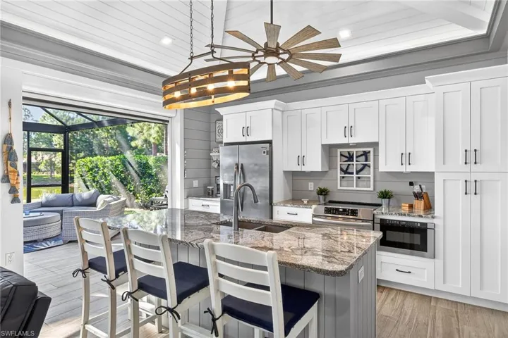 Kitchen featuring light stone counters, stainless steel appliances, a kitchen breakfast bar, light wood-type flooring, and white cabinetry