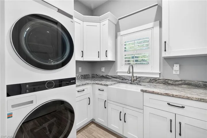 Laundry area with estacked washer and dryer, cabinet space, and light wood-style floors