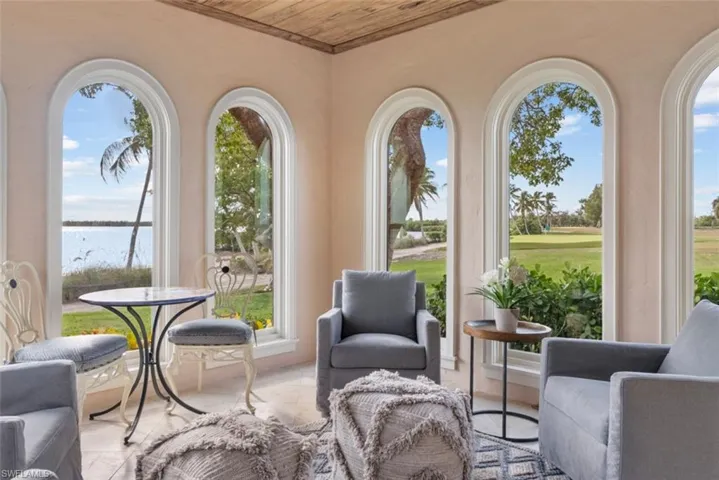 MAIN HOUSE -Living area featuring several arched windows providing views of a body of water, green lawns, and palm trees