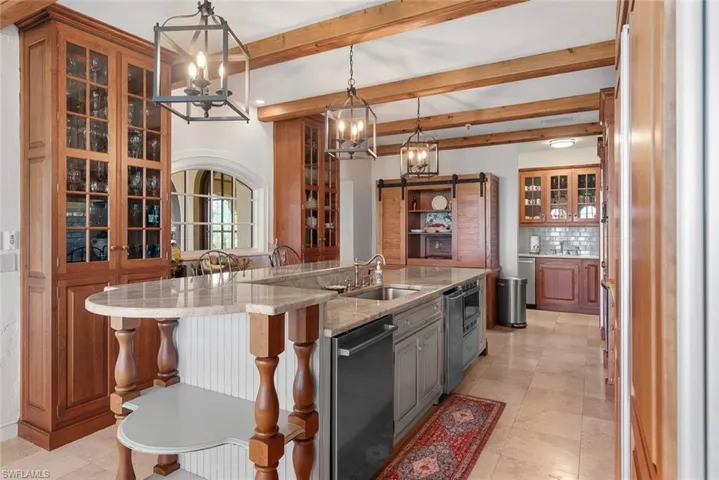 MAIN HOUSE -Kitchen featuring exposed wooden beams, a large island with a double sink and stone countertop, and custom cabinetry