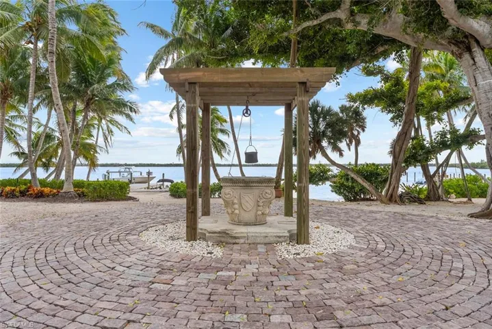 The property features a circular paver drive, a decorative stone well, and mature palm trees