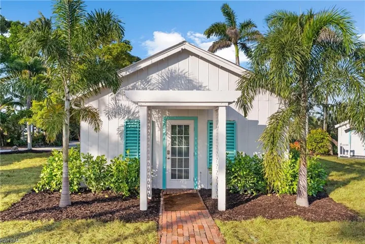 GUEST COTTAGE #4 - The property features a white exterior with a peaked roof, accentuated by vibrant turquoise shutters and a matching front door with glass panels