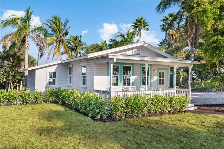GUEST COTTAGE #4 The property features a charming front porch with white railings and teal accents, surrounded by a well-maintained lawn and lush green shrubbery