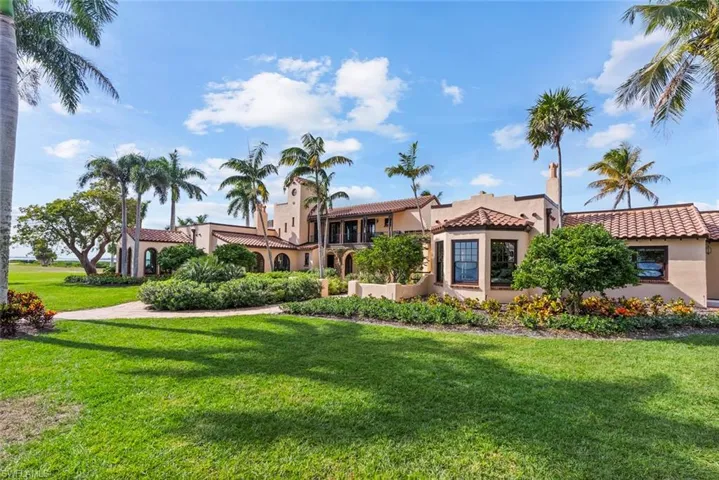 MAIN HOUSE - The property features a Spanish Colonial style exterior with a tiled roof, bay windows, and an extensive lawn with mature palm trees and manicured landscaping
