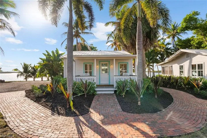 GUEST COTTAGE #1 - This charming property features a white exterior with a turquoise trim, a welcoming covered porch, and a brick pathway