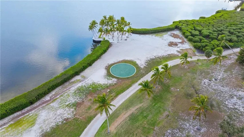 HELIPAD AND PALM GROVE - Aerial view of the property's waterfront access, featuring a private sandy area, mature palm trees, and a circular green feature