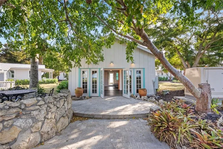 GUEST COTTAGE #4 BACK - The property features white vertical siding and double French doors with light blue accents, opening onto a paved patio