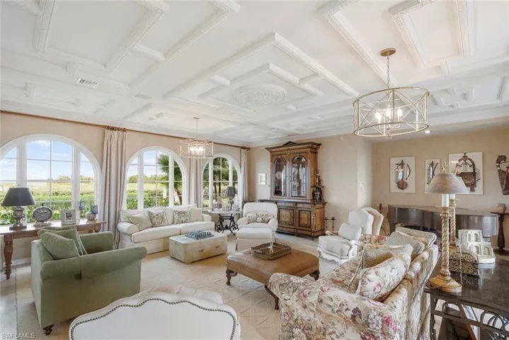 MAIN HOUSE -This inviting living space features arched windows with views of greenery, a coffered ceiling, and a decorative chandelier